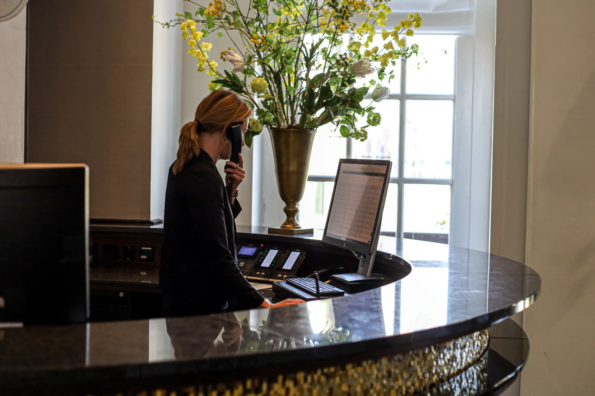Receptioniste verwelkomt gast aan marmeren balie met bloemen

